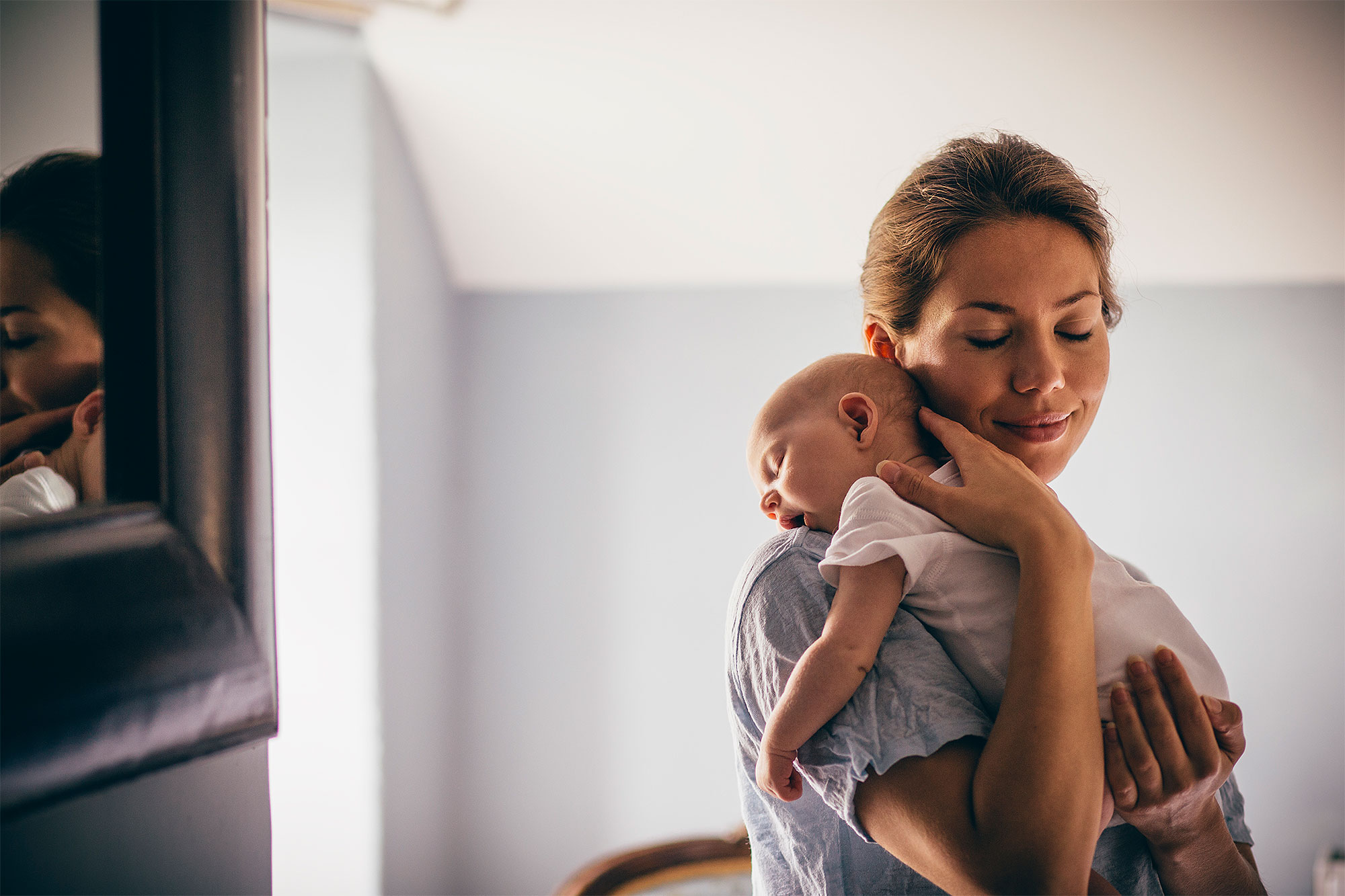 A happy new mother smiles as she craddles her sleeping baby in her arms. She has her eyes closed as she holds her close.